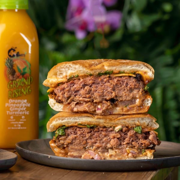 A C4Eats vegan burger, cut in half, revealing the patty, sauce, and toppings, with a juice bottle.