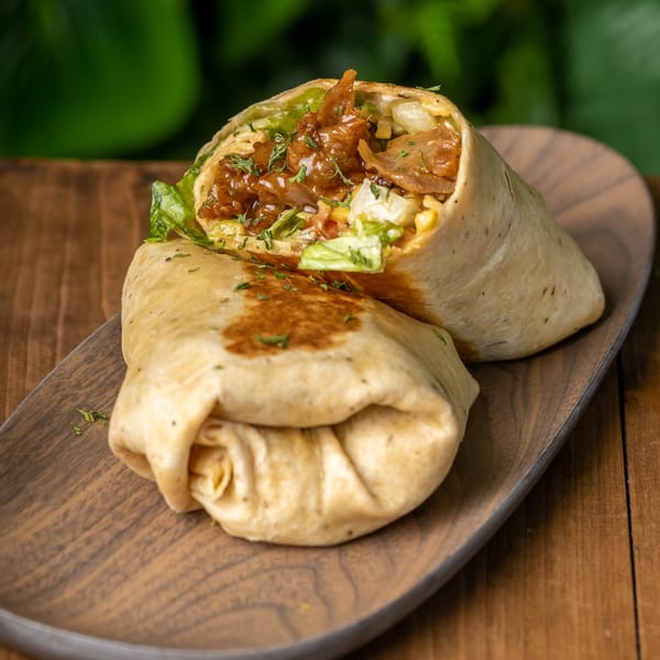 Two halves of a vegan wrap filled with saucy plant-based meat and fresh lettuce on a wooden platter.