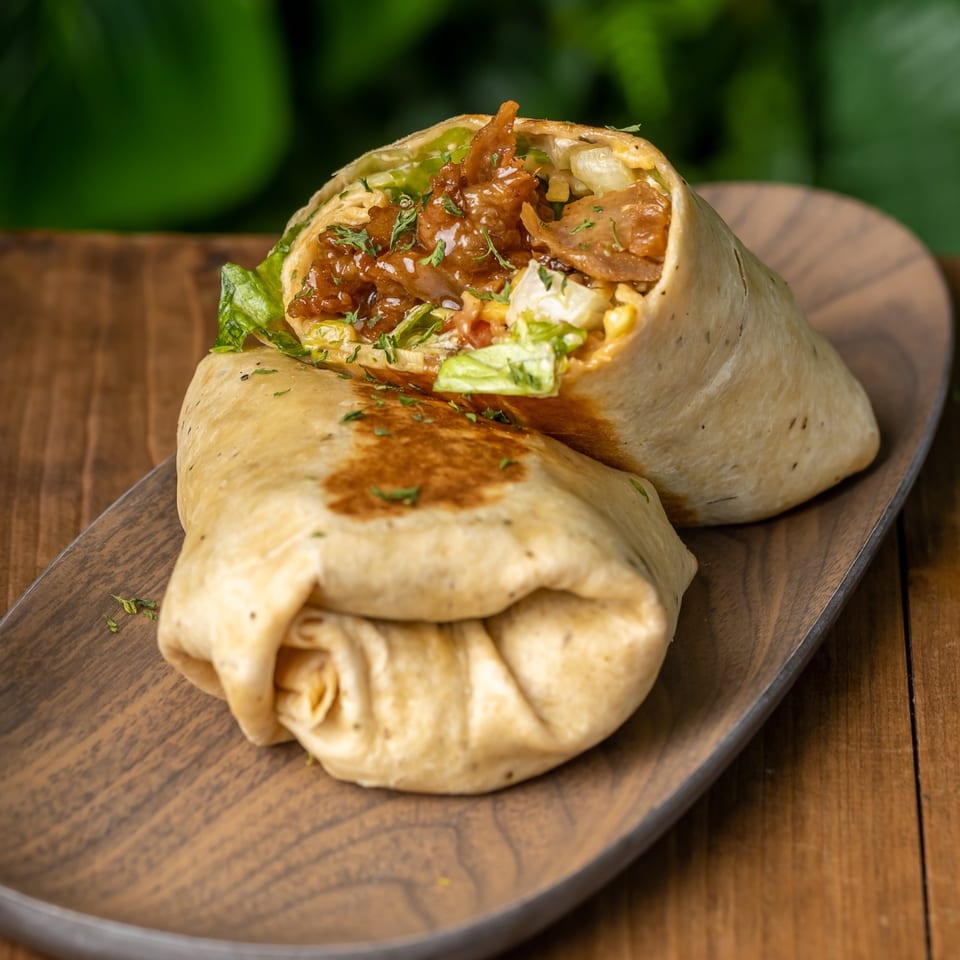 Two halves of a vegan wrap filled with saucy plant-based meat and fresh lettuce on a wooden platter.