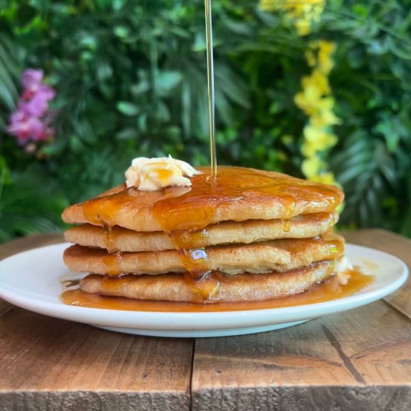 Vegan pancakes with butter and syrup drizzling over them, against a lush green background.